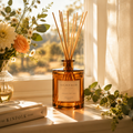Golden Hour Reed Diffuser in an amber glass bottle with rattan reeds on a sunlit windowsill